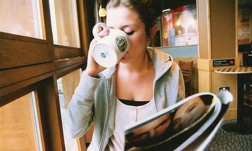 девушка читает журнал и пьет из кружки Стар Бакс