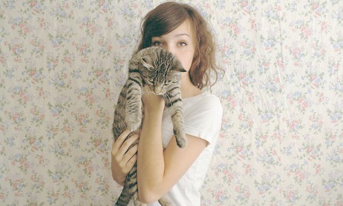 девушка в белой футболке у стены с полосатым котом на руках