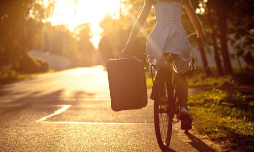 девушка едет на велосипеде с чемоданом в руке