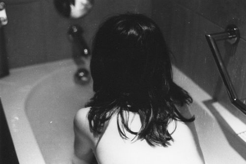 Брюнетка сидит в ванной со спины без лица