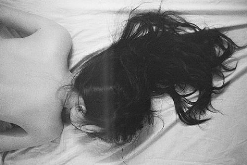 Брюнетка лежит лицом в постели разложив длинные волосы