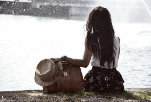 Девушка сидит на берегу с сумкой и шляпкой