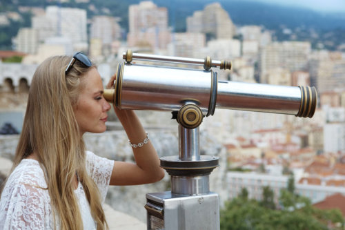 Блондинка с длинными прядями смотрит в подзорную трубу на смотровой площадке