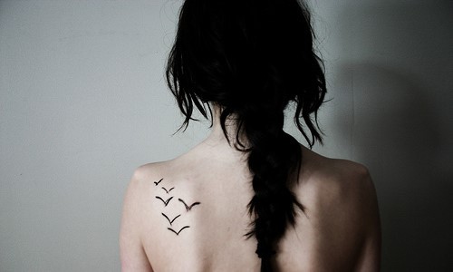 Черные волосы у девушки с татуировкой чаек на лопатке