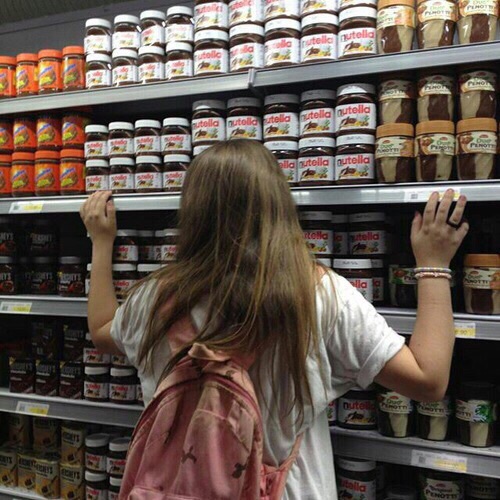 девушка со спины обнимает полку в магазине с шоколадной пастой Nutella