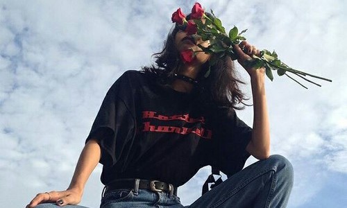 девушка в черной футболке и джинсах прикрыла лицо букетом красных роз