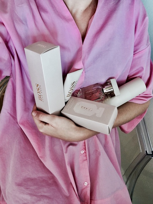 девушка в розовой рубашке с коробочками косметики и парфюмом