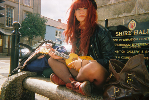 рыжая девушка с укулеле на каменной скамье в городе