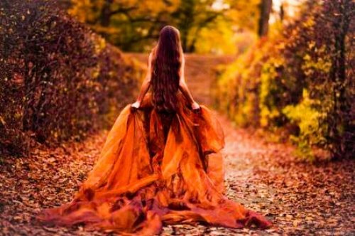 девушка в оранжевом платье с очень длинными волосами со спины без лица идет по осенней аллее