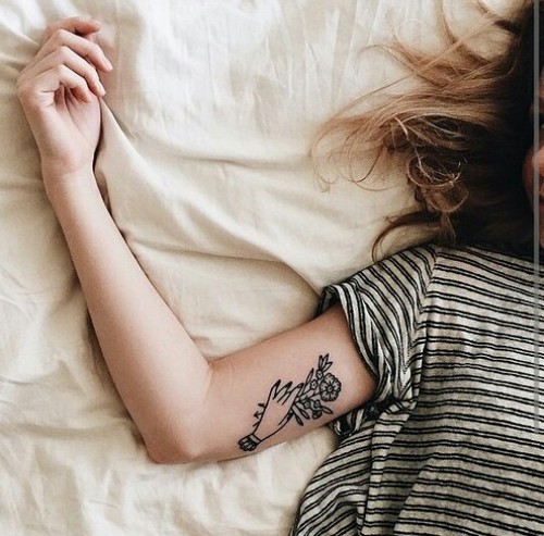 девушка в полосатой футболке без лица с татуировкой лежит в кровати