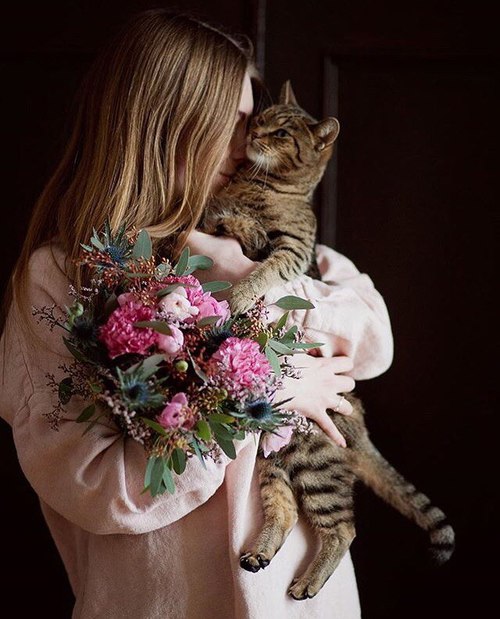 русая девушка обнимает полосатую кошку с букетом весенних цветов