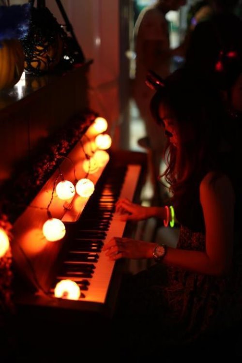 девушка играет на пианино с гирляндой и неоновыми браслетами