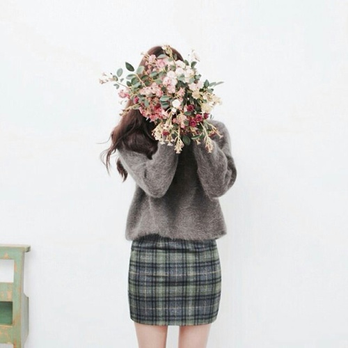 девушка прикрыла лицо букетом цветов в короткой юбке и свитере