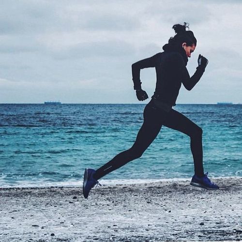девушка в черном спортивном костюме на утренней пробежке вдоль моря