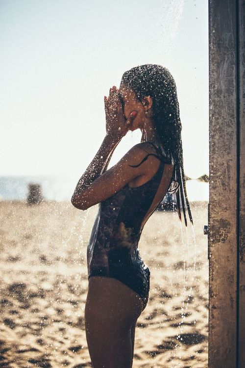 девушка в брызгах воды душа на пляже без лица