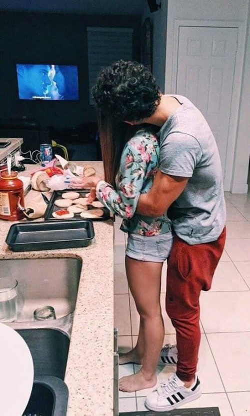 влюбленные обнимаются на кухне делая вкусняшки перед телевизором