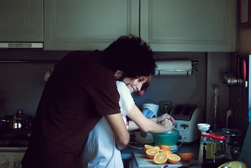 влюбленные готовят апельсиновый фреш обнимаясь на кухне