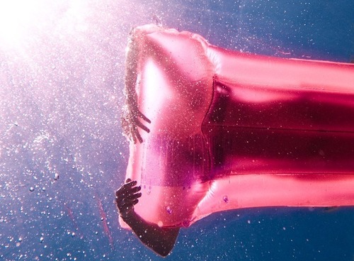 девушка на розовом надувном матрасе в лучах солнца вид из под воды