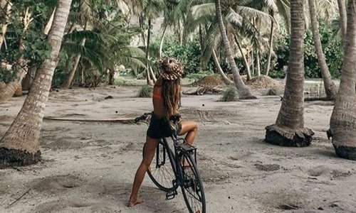девушка без лица со спины катается на велосипеде среди пальм