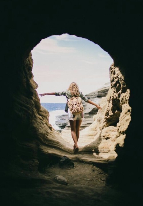 девушка со спины вышла с пещеры с рюкзаком к морю
