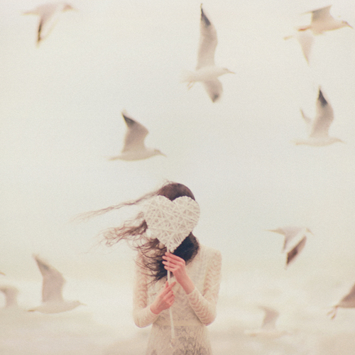 девушка прячет лицо за сердечком на палочке вокруг летают чайки