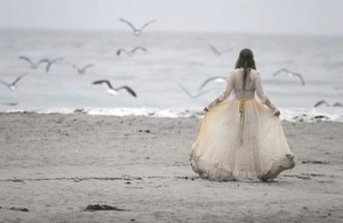 девушка в грязном свадебном платье идёт по берегу вокруг летают чайки