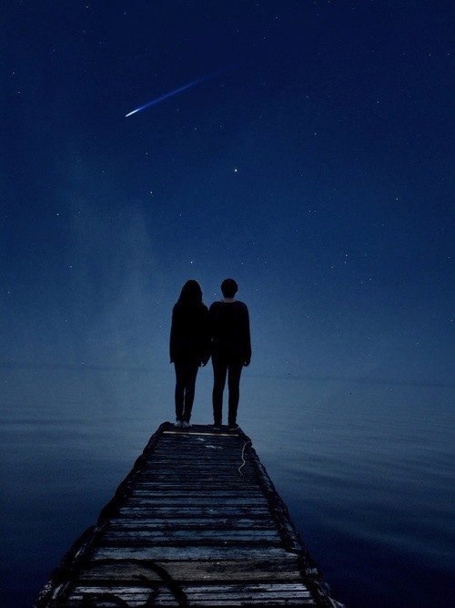 двое на пирсе смотрят на падающую звезду, загадывая желание