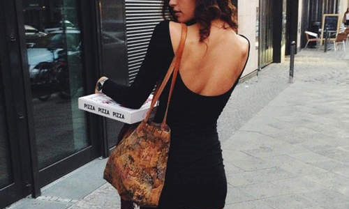 девушка в маленьком черном платье несет пиццу оборачиваясь