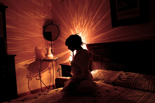 силуэт девушки сидящей на кровати в темной комнате освещаемой ночником