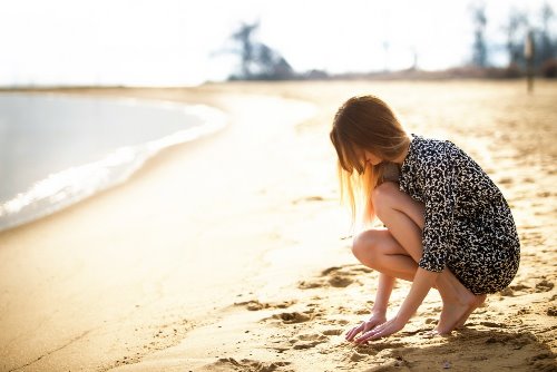 дівчина навприсядки згрібає пісок на пляжі