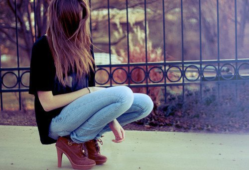 девушка в черной футболке и джинсах без лица на корточках у забора