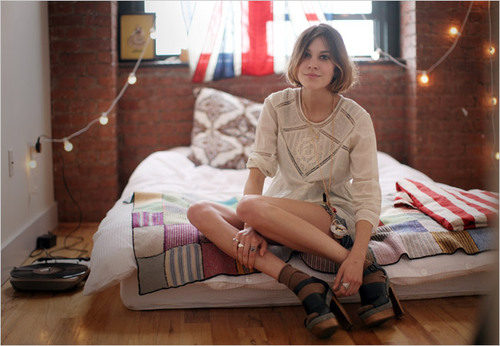 дівчина з довгими ногами сидить на надувному матраці на підлозі в кімнаті з гірляндами стіни з цегли