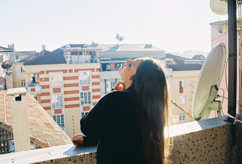 дівчина спиною на балконі з телевізійної тарілкою насолоджується сонечком