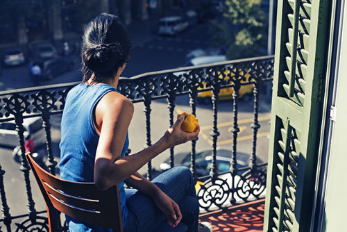дівчина з чорним волоссям зі спини їсть яблуко сидячи на балконі в сонячний день