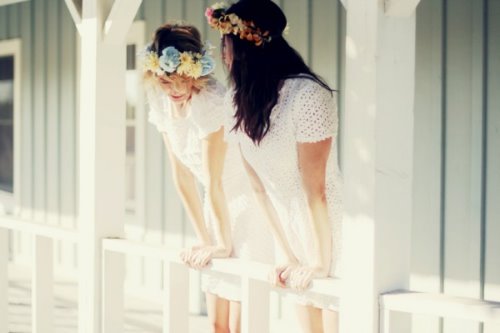 две подружки в белых платьях и венках выглядывают с балкона вниз