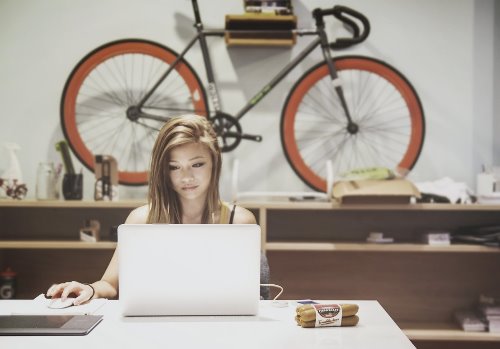 девушка с русыми волосами работает за ноутбуком на стене висит велосипед