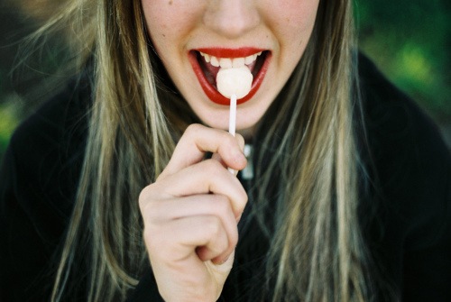 девушка с белыми зубами и красными губами кусает конфету