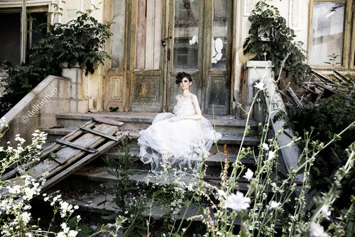 дівчина в білому платті сидить на сходинках зруйнованого будинку у дворі