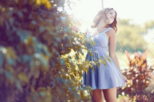 дівчина в блакитному короткому літньому платті позує біля кущів у дворі будинку