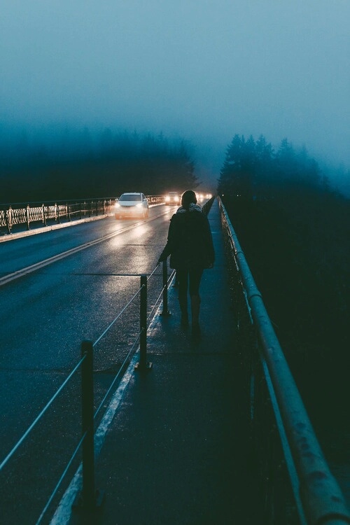 девушка идёт по мосту в свете фар ночного города