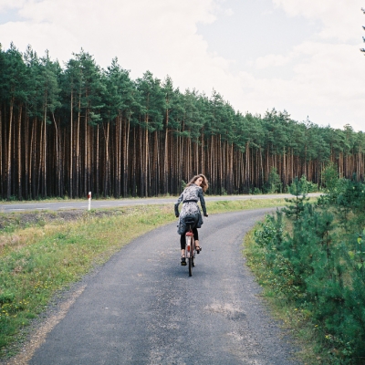 девушка едет на велосипеде оглядывается со спины в хвойном лесу