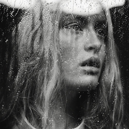 светловолосая девушка за окном покрытым каплями дождя