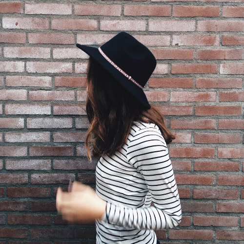 девушка в шляпе у стены в полосатой кофте