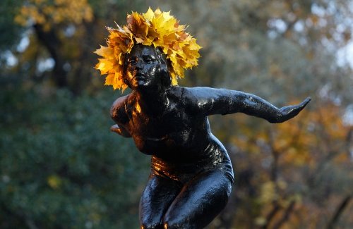 памятник женщины в вышной короне из осенних кленовых желтых листьев