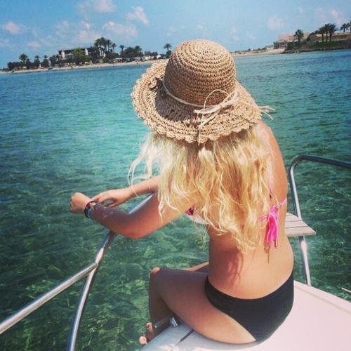 блондинка в соломенной шляпке спиной в купальнике на носу лодки