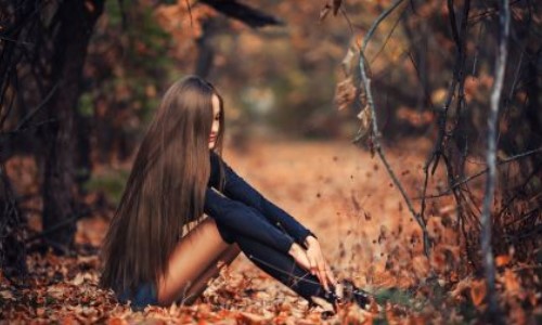 девушка с длинными русыми волосами сидит в листьях осенью в парке