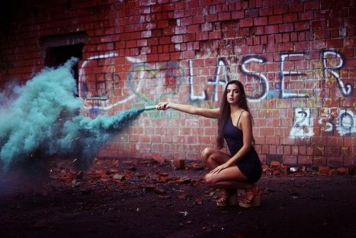 девушка под стеной пускает синий дым