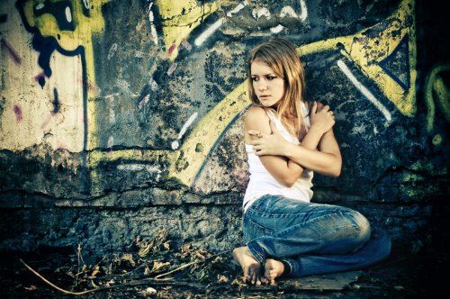 девушка в белой майке и джинсах сидит под стеной разрисованной граффити