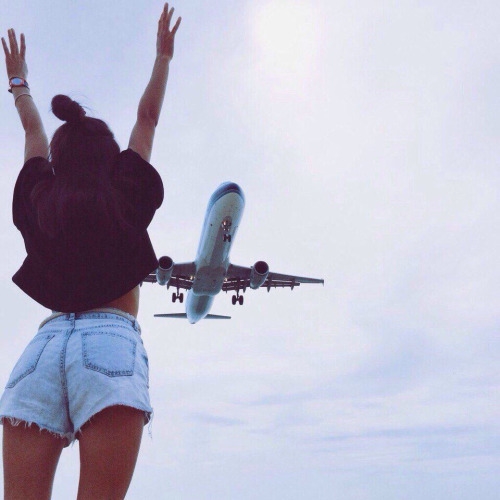 девушка в коротких джинсовых шортах спиной встречает самолет в небе
