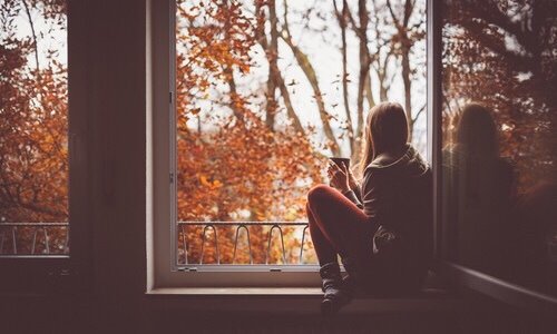 девушка с кружкой сидит на подоконнике за окном желтые листья осени не видно лица